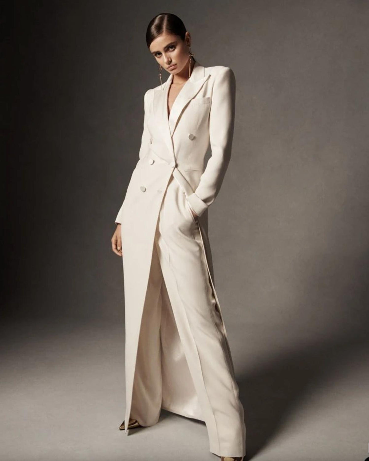 Model wearing a pristine white Wolfsburg suit set with a long, double-breasted blazer and matching wide-leg trousers.