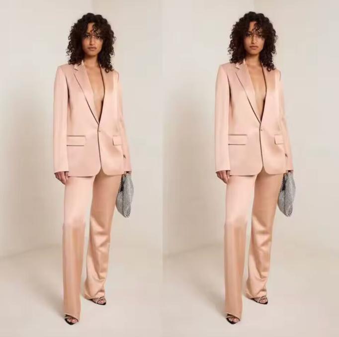 Woman wearing a sleek, blush pink satin two-piece suit with a single-button notch lapel jacket and tailored trousers.