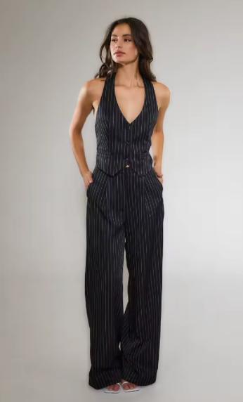 Woman wearing a black pinstriped two-piece suit with a V-neck vest and tailored wide-leg trousers.