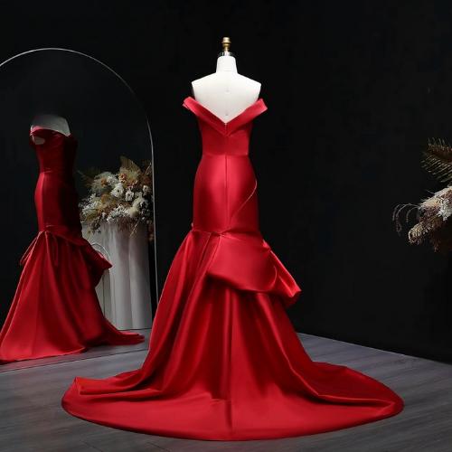 Red satin off-shoulder mermaid evening gown with elegant draping and a dramatic train on a mannequin.