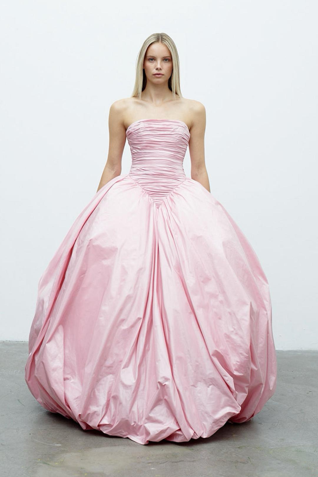 Strapless pink taffeta A-line gown with a ruched bodice and voluminous, draped floor-length skirt.