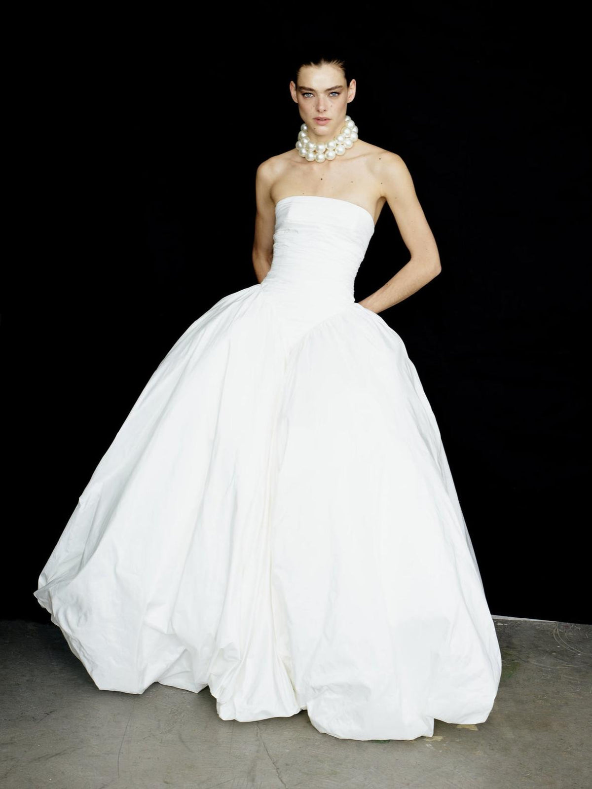 Strapless white taffeta A-line gown with a ruched bodice and full skirt, styled with a chunky pearl necklace.