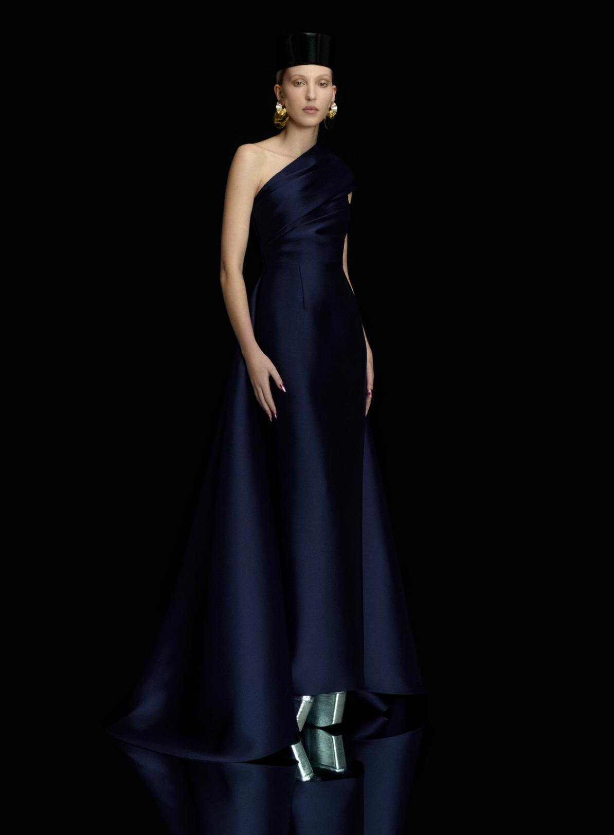 Navy blue satin one-shoulder gown with a fitted waist, pleated bodice, and dramatic high-low A-line skirt.