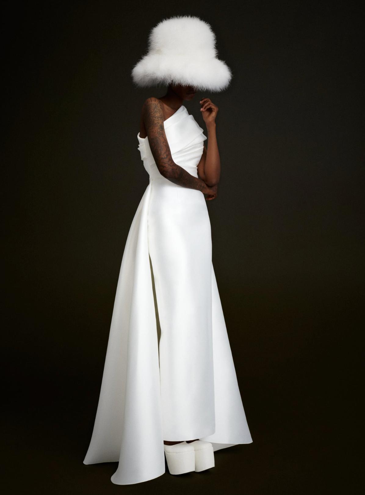 White satin one-shoulder Tallulah gown with an A-line skirt and draped bodice, paired with a matching fluffy white hat.