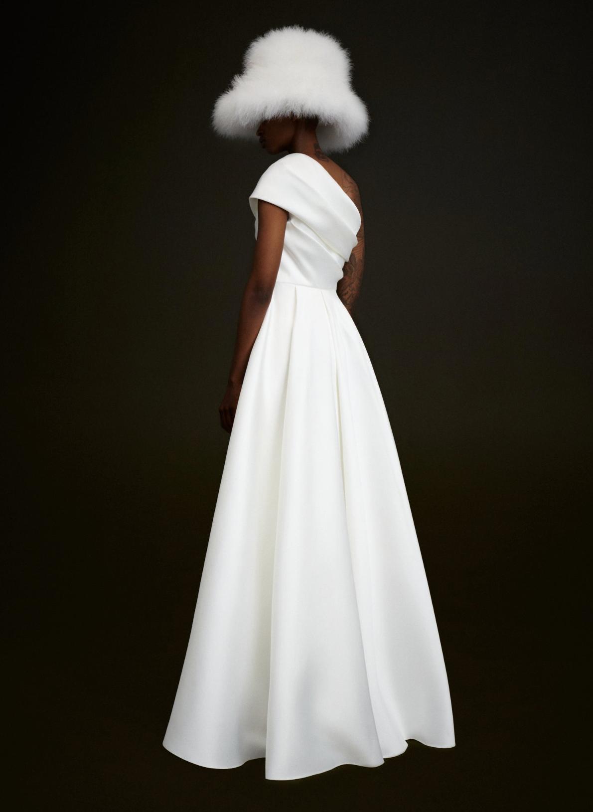 White satin one-shoulder A-line gown with a fitted waist and draped bodice, styled with a fluffy white hat.