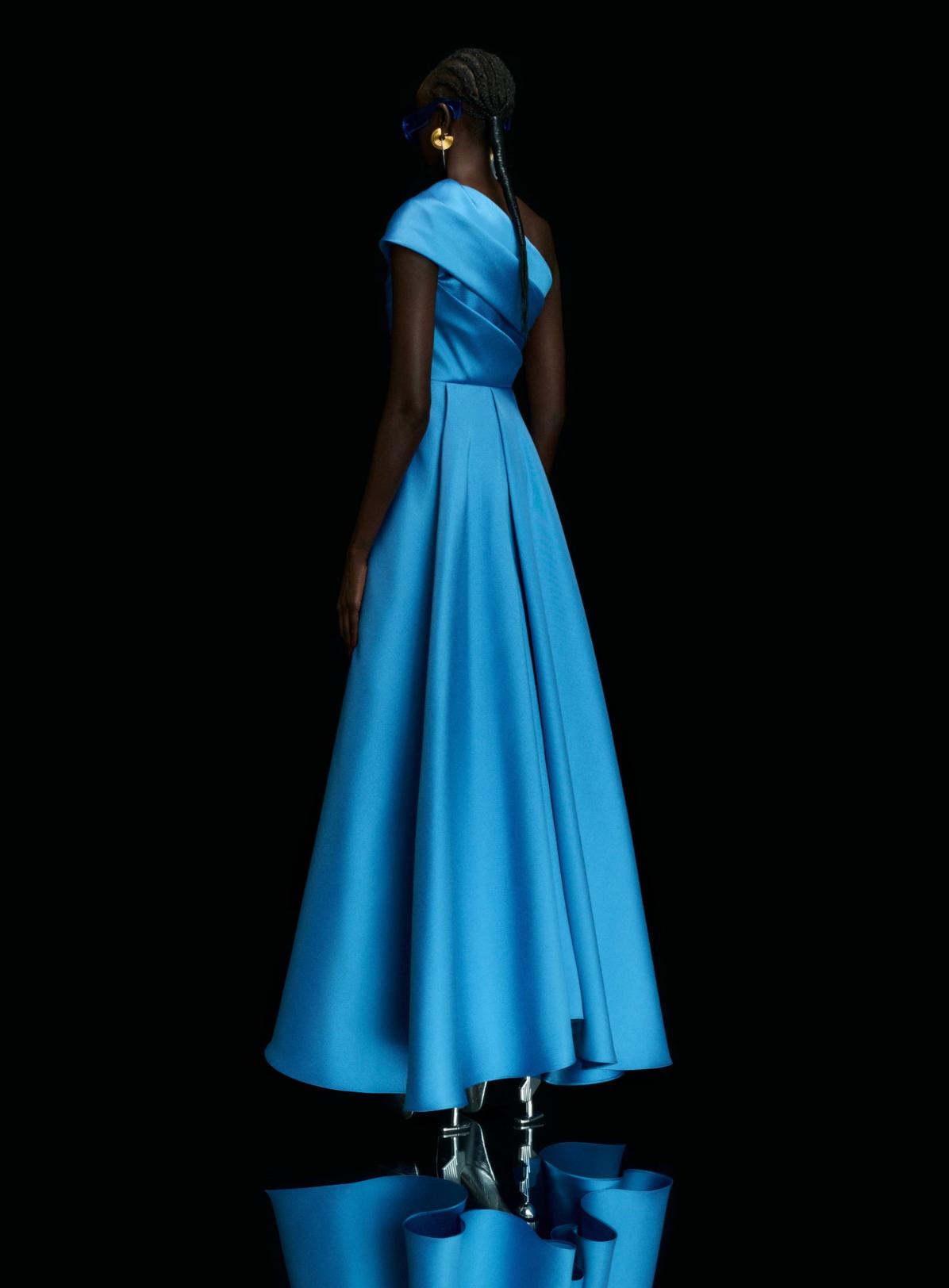Bright blue satin one-shoulder A-line gown with a fitted waist and dramatic high-low hem against a black background.