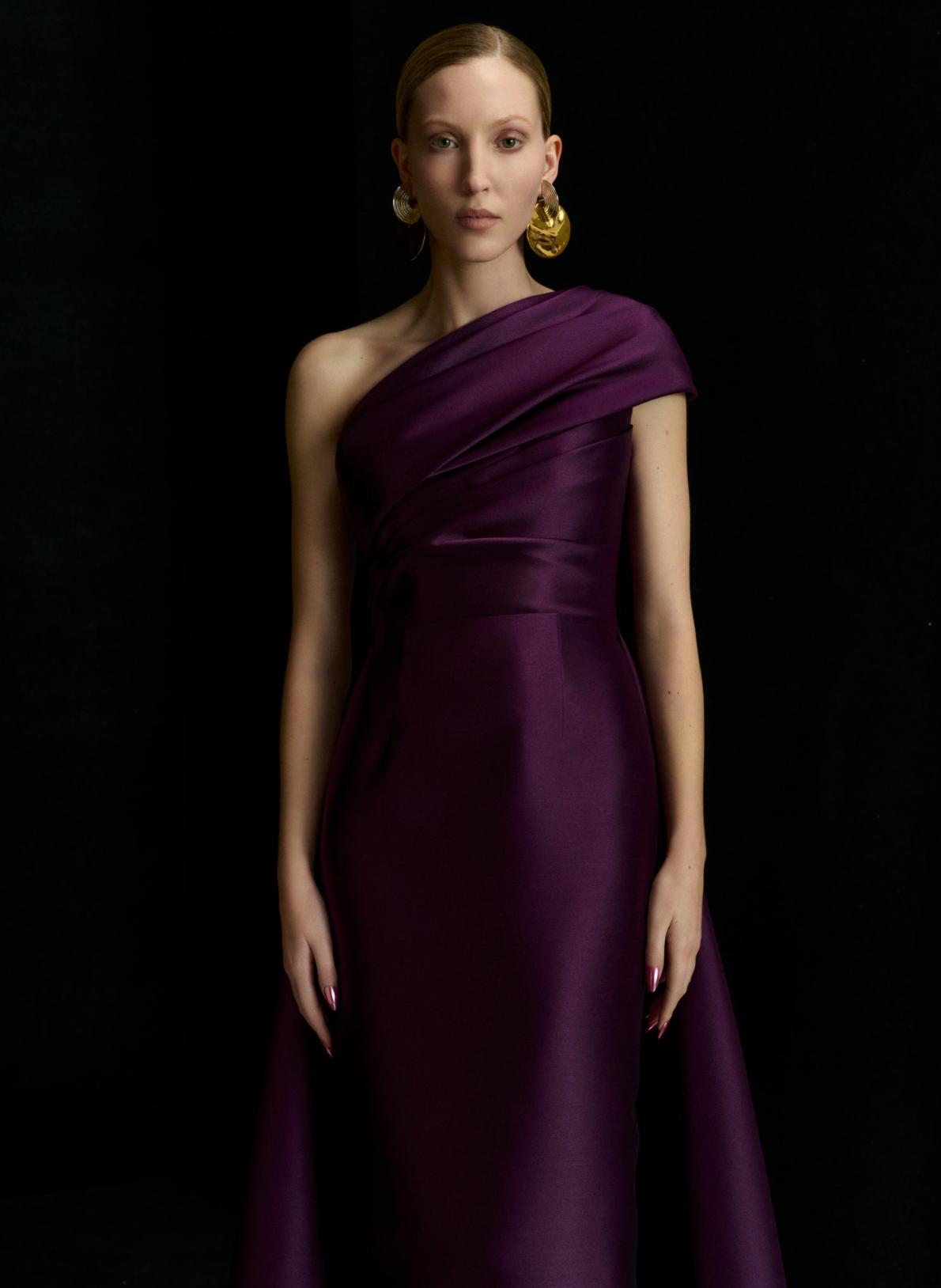 Elegant one-shoulder purple satin gown with draped bodice and A-line silhouette against a black background.